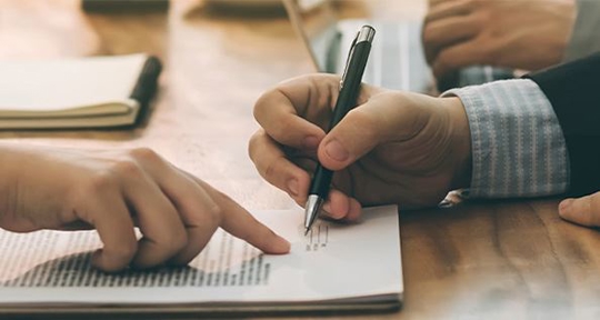 a person pointing at a paper and a person writing down on a paper